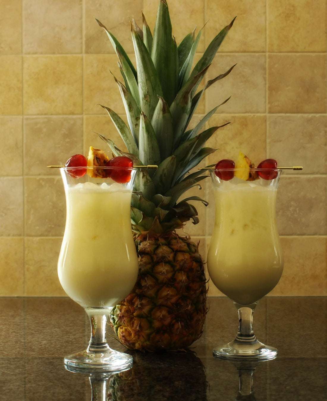 Pina Colada spiced rum cocktail made with Swan Knight Distillery golden spiced rum, in 2 Hurricane glasses with a whole pineapple back drop