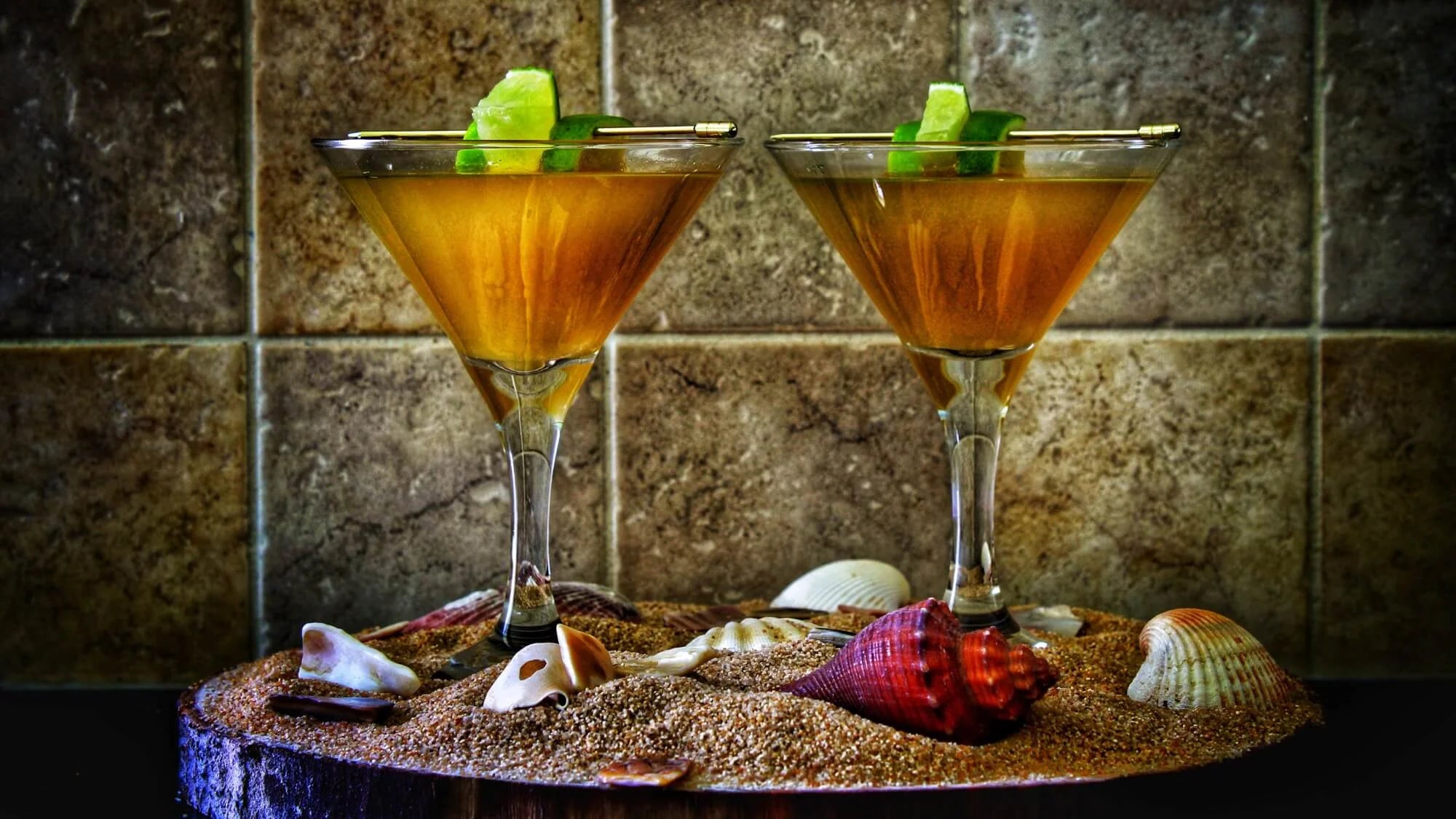 2 pineapple daiquiris in martini glasses, with a sand and shell backdrop